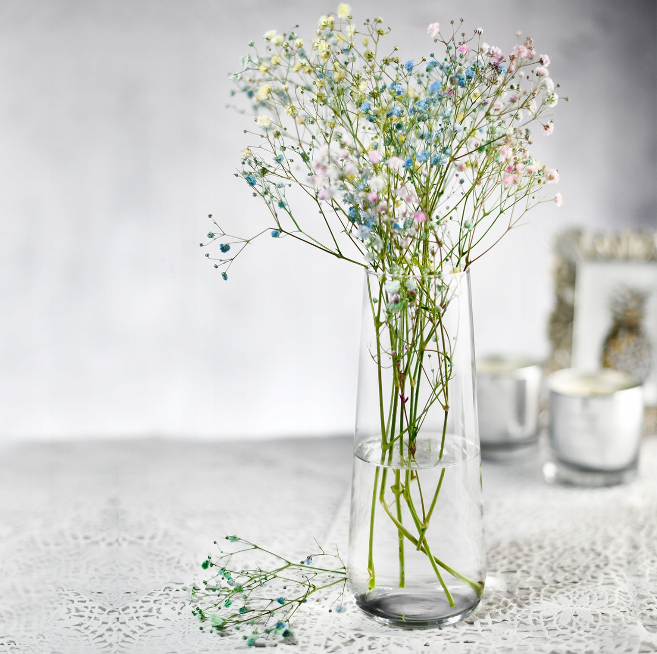 Elegant høy glassvase med blomster på blondeduk i interiør