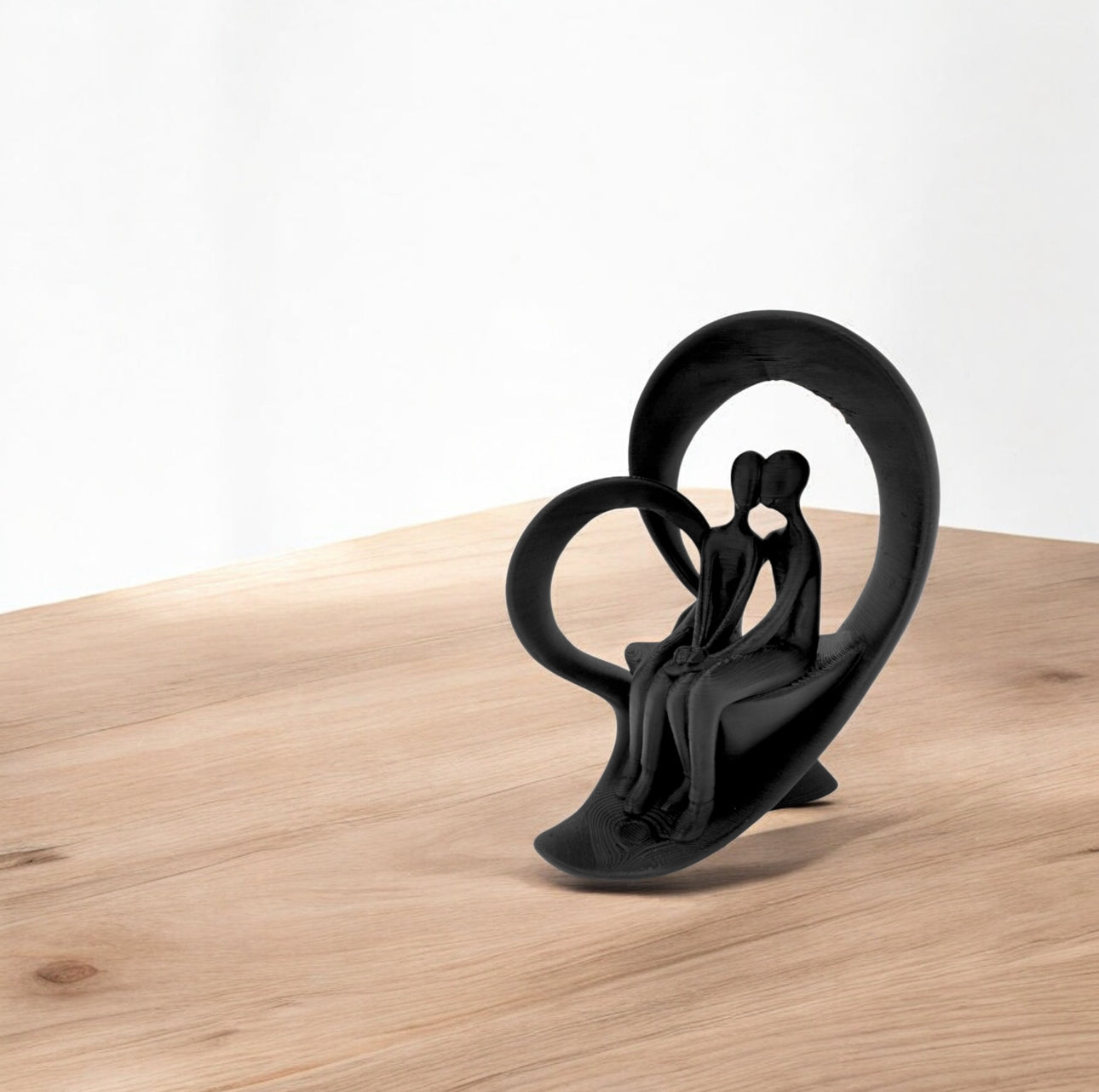 Svart kunstskulptur av par i hjerteform på lyst tregulv