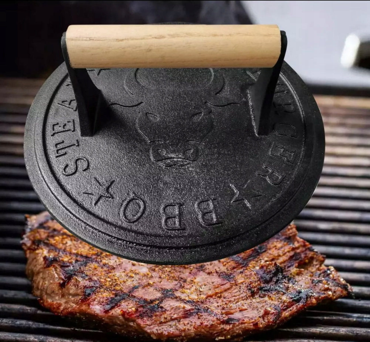 Grillpresse i støpejern brukes til å presse kjøtt på grill, omgitt av glødende grillriller