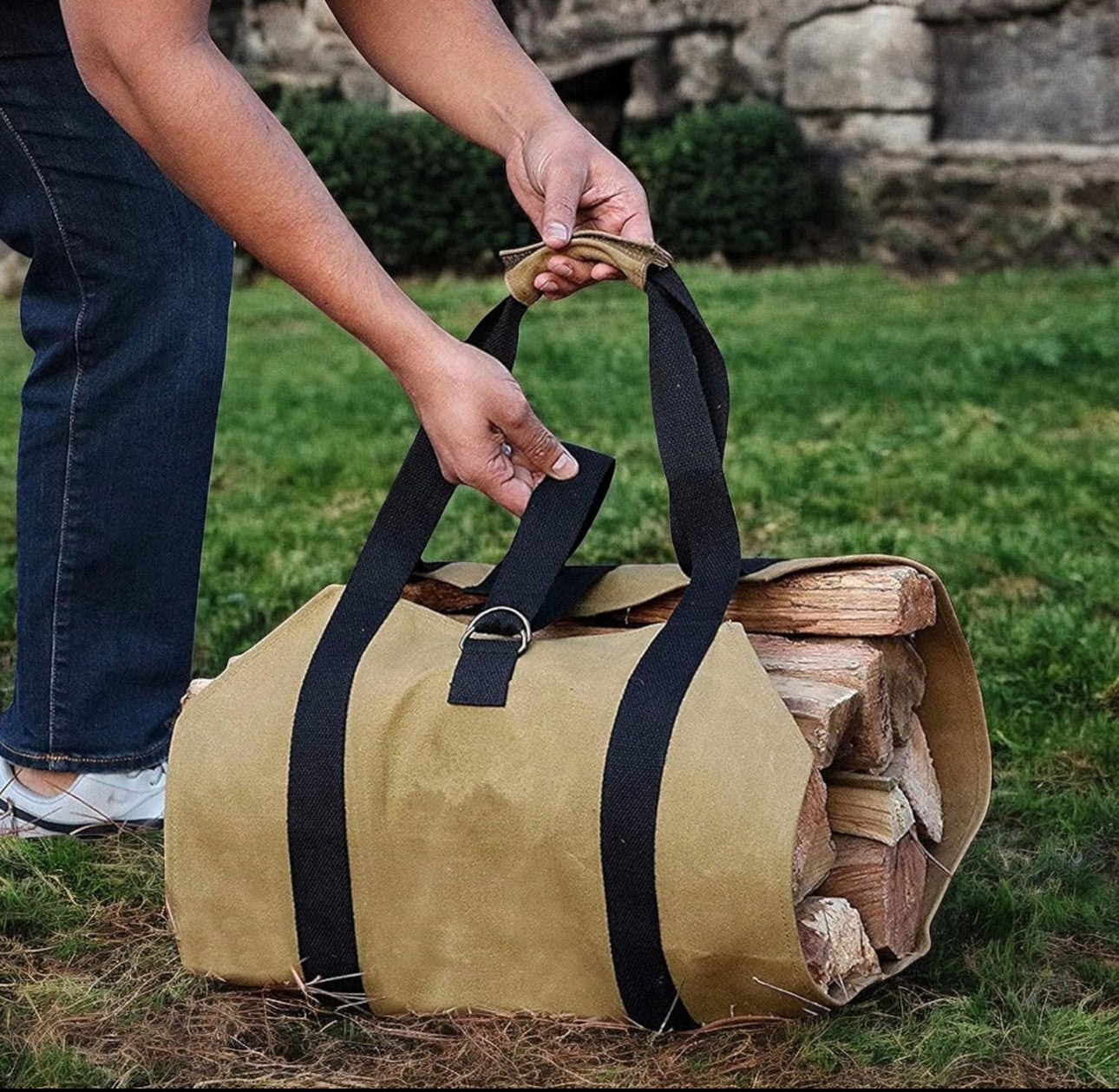 Person løfter beige vedbag i lerret med svarte håndtak fylt med vedkubber