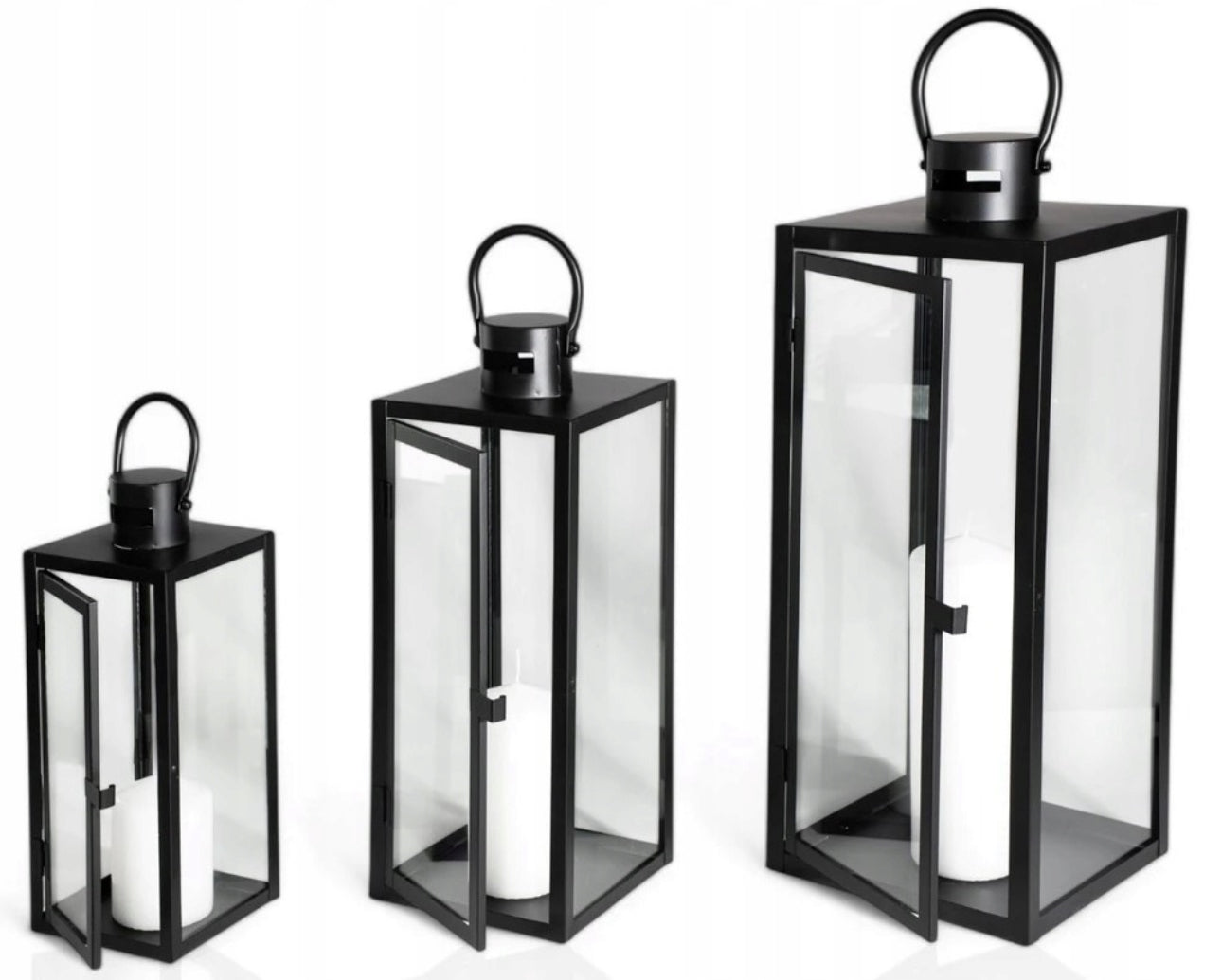 Tre svarte lyslykter i metall og glass med hvite kubbelys, plassert i ulike høyder på hvit bakgrunn