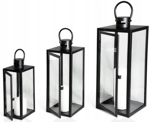 Tre svarte lyslykter i metall og glass med hvite kubbelys, plassert i ulike høyder på hvit bakgrunn