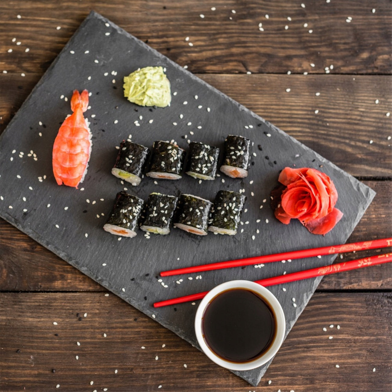 Svart skiferbrett med sushi, soyasaus og røde spisepinner