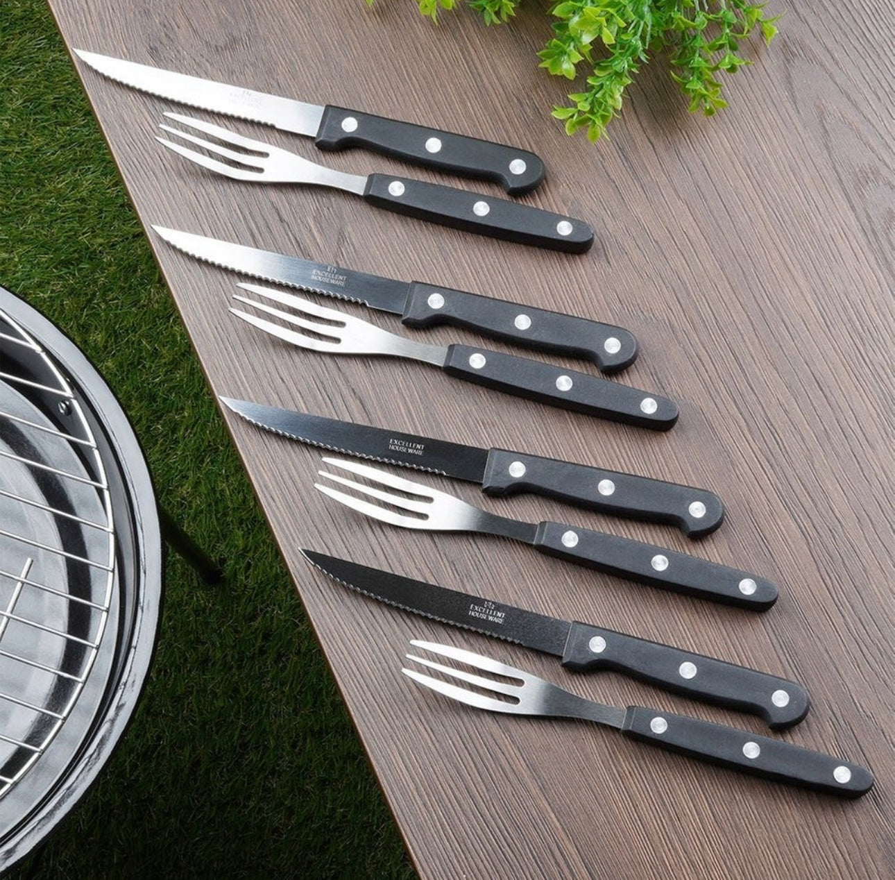 Stekebestikk med svarte håndtak lagt på trebord ved siden av grill og planter
