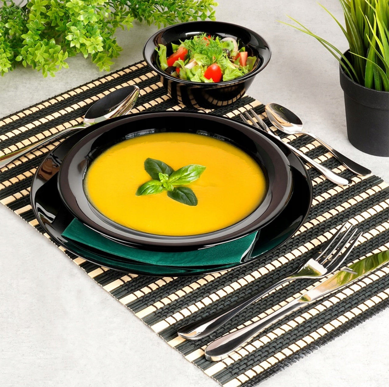 Dyp svart tallerken med gresskarsuppe og salatbolle i matchende design på elegant dekket bord