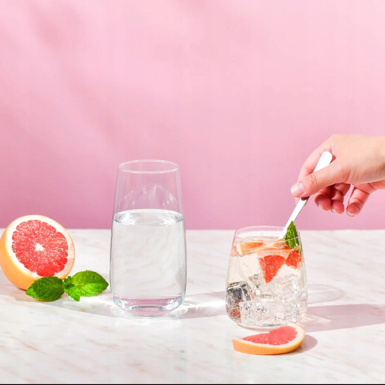 To moderne glass, ett med vann og ett med drink med grapefrukt og isbiter