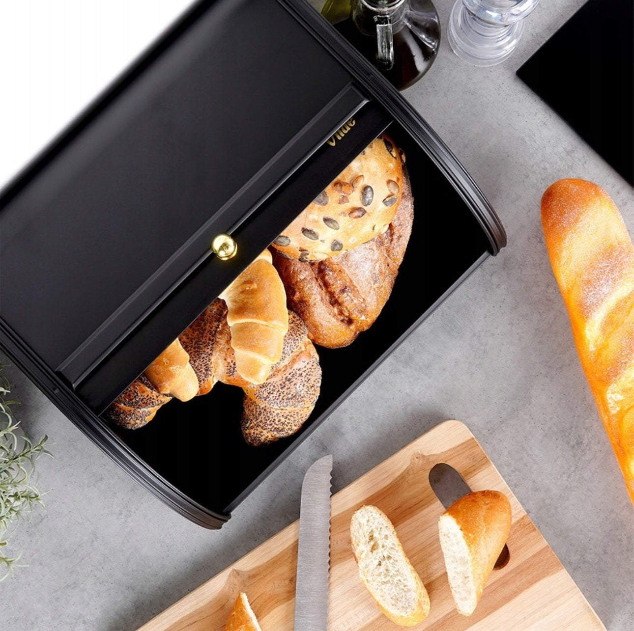 Brødboks med croissanter og rundstykker sett ovenfra på lys kjøkkenbenk