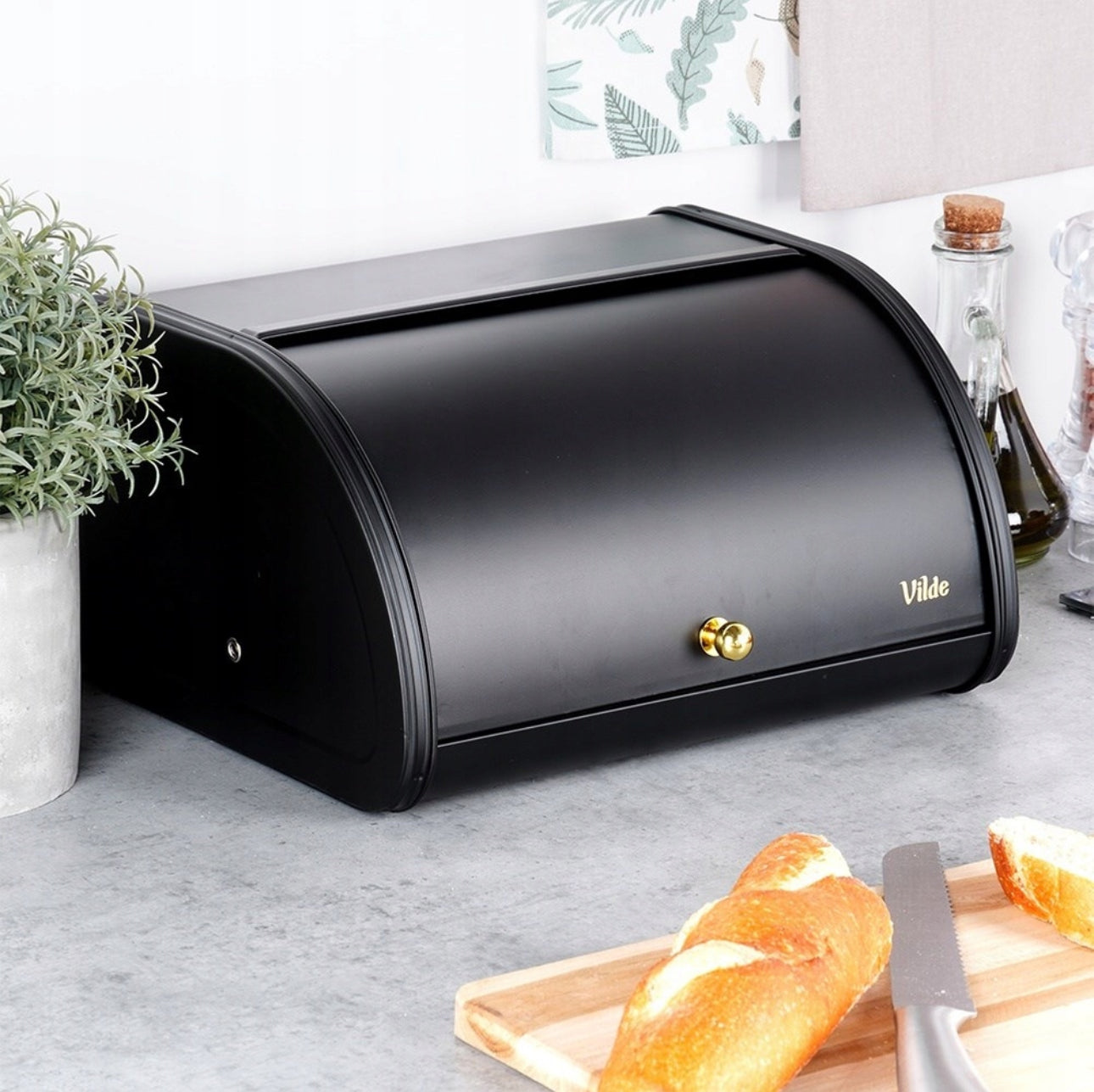 Elegant brødboks i svart stål plassert på kjøkkenbenk med urter og bakverk