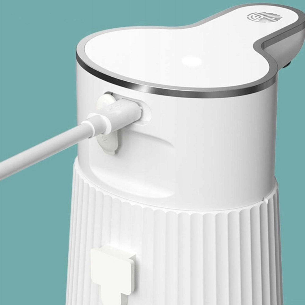 USB-C kabel koblet til baksiden av hvit berøringsfri såpedispenser mot grønn vegg