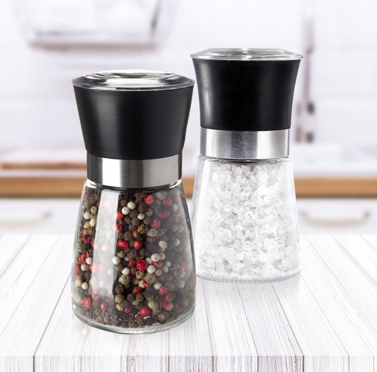 Elegante salt- og pepperkverner i glass med sort topp og stål, plassert på lys kjøkkenbenk.