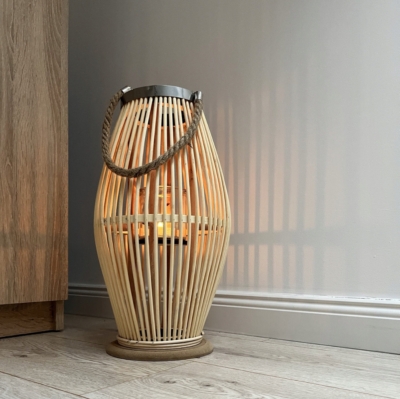 Beige bambuslyslykt plassert ved vegg og møbel, gir varm belysning mot grå vegg