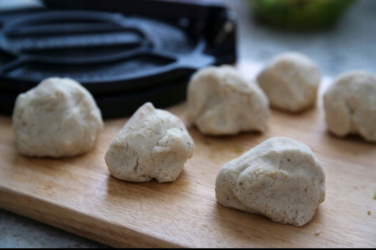 Ferske maismel-deigkuler på trefjøl foran tortilla-presse i bakgrunnen