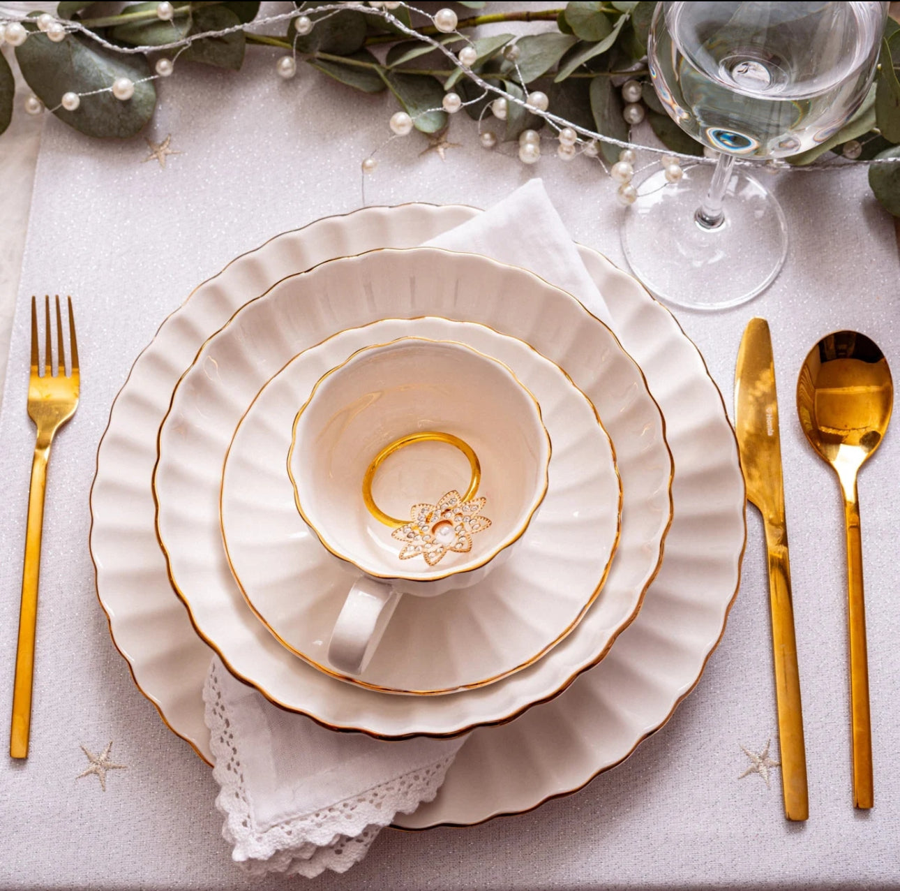Elegant borddekking med hvit desserttallerken, middagstallerken og kopp med gullkant, gullbestikk og serviett