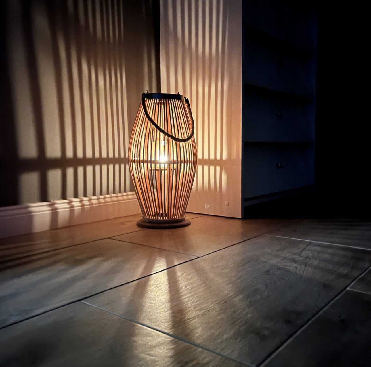 Bambuslyslykt med tent lys i mørkt hjørne, skaper stemningsfullt skyggespill