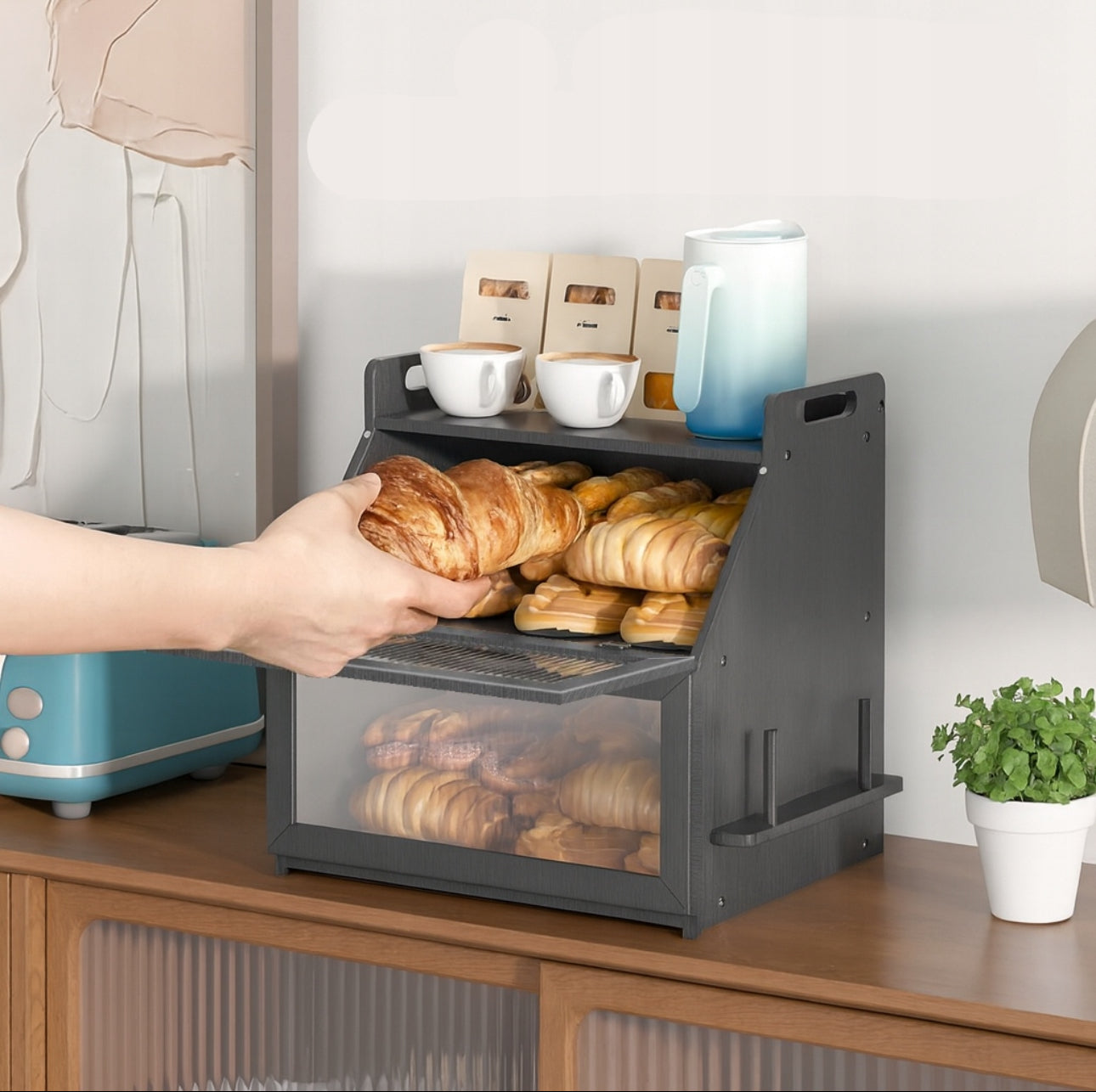 Hånd tar ut croissant fra svart brødboks i bambus med to hyller