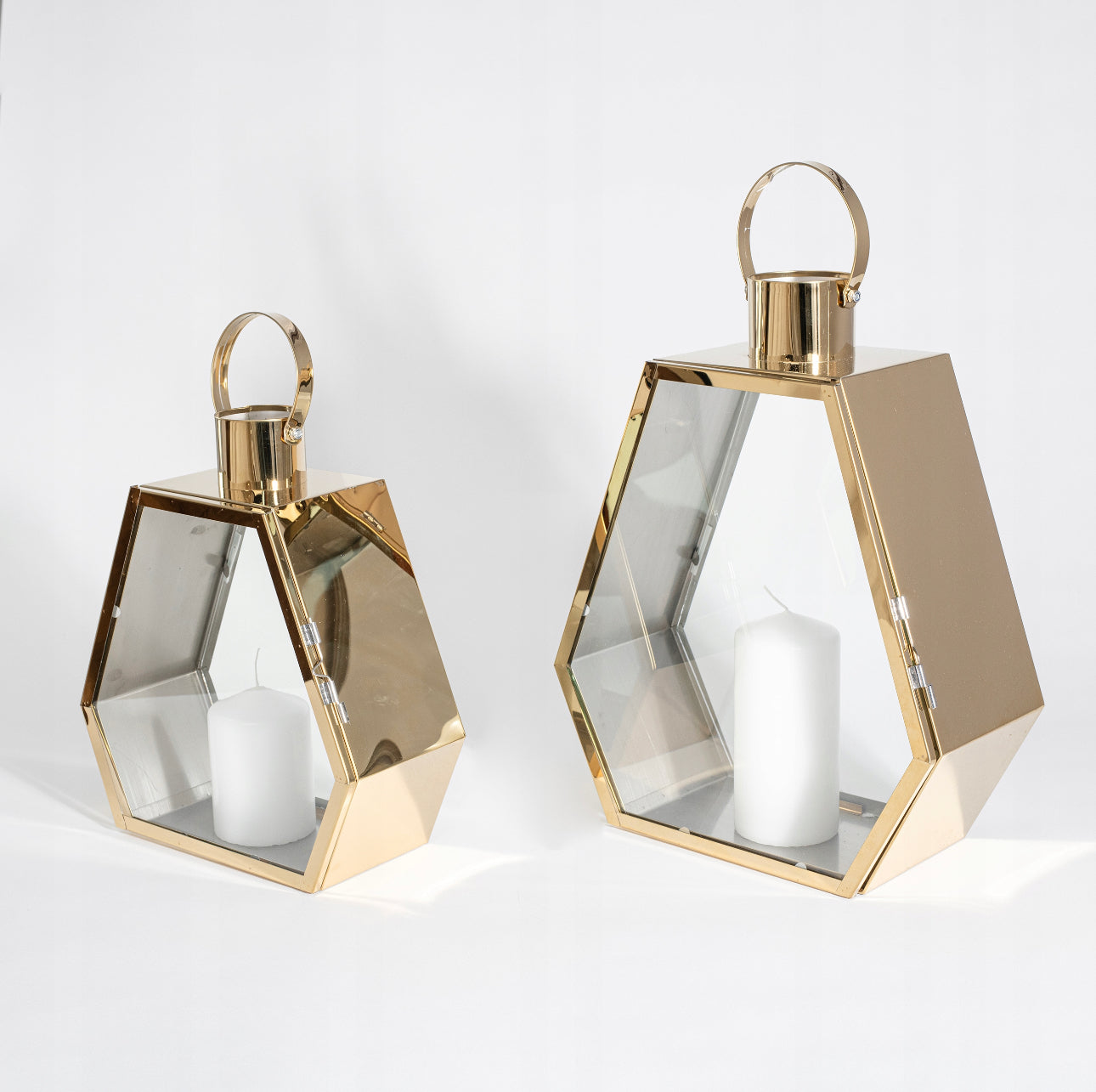 Elegant lyktesett i gull og glass med hvite kubbelys, mot hvit bakgrunn i studiolys