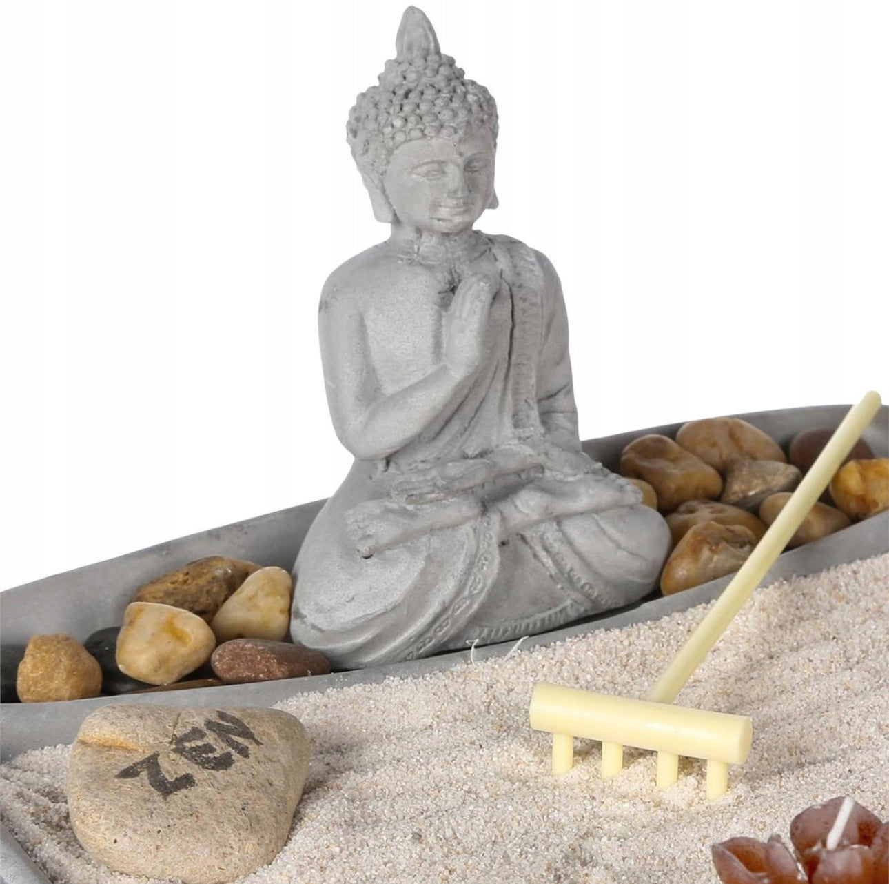 Detalj av Buddha-statuett i grå keramikk omgitt av sand, småstein og miniatyr rake