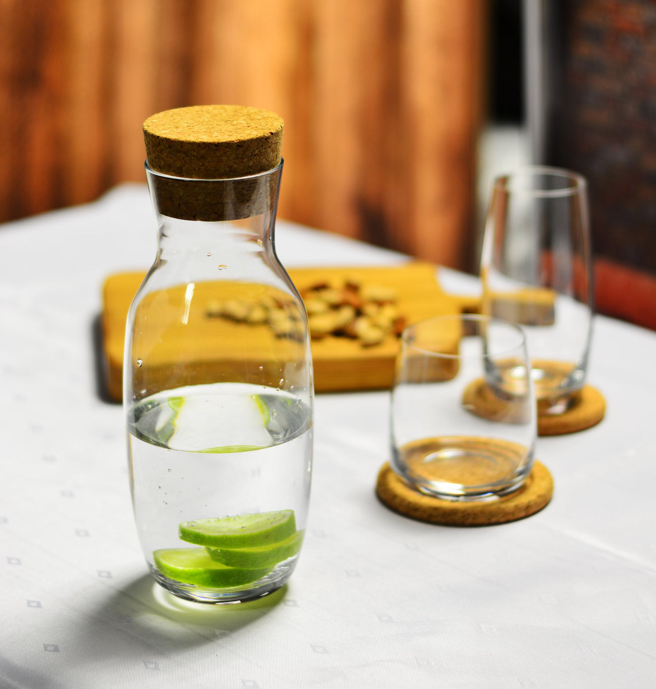 Glasskaraffel med kork og lime på bord med drikkeglass og nøtter