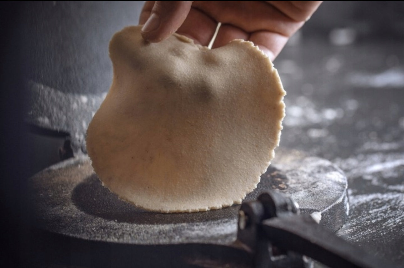 Tynn, ferskpresset tortilla holdes opp foran tradisjonell stekeflate i støpejernspresse