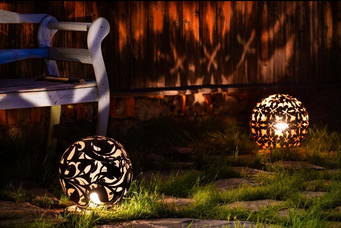 Opplyst cortenstål-lampe i hagen om natten med lysskygger på vegg