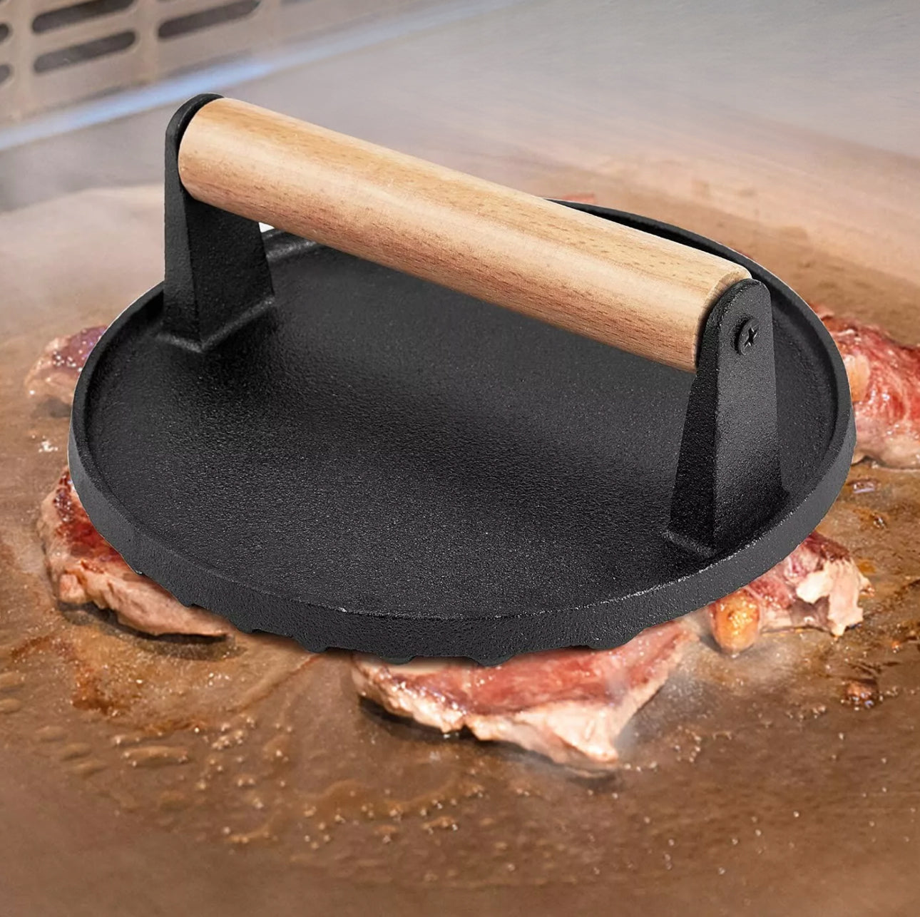 Støpejernspresse med trehåndtak ligger på kjøttstykker som stekes på grillplate