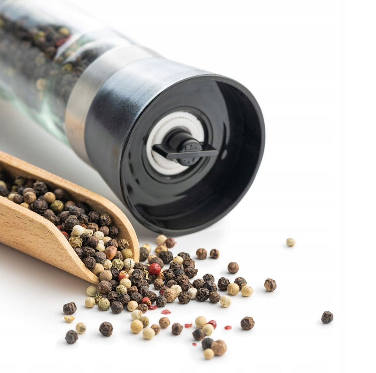 Nærbilde av pepperkvern med keramisk kvernmekanisme og løse pepperkorn på hvit bakgrunn.