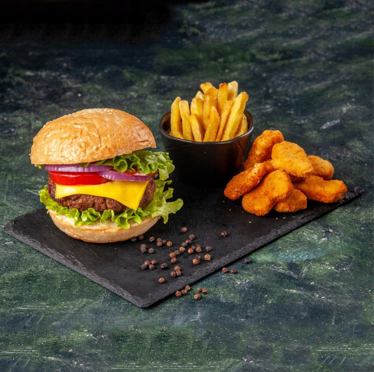 Svart skiferbrett med burger, pommes frites og kyllingnuggets