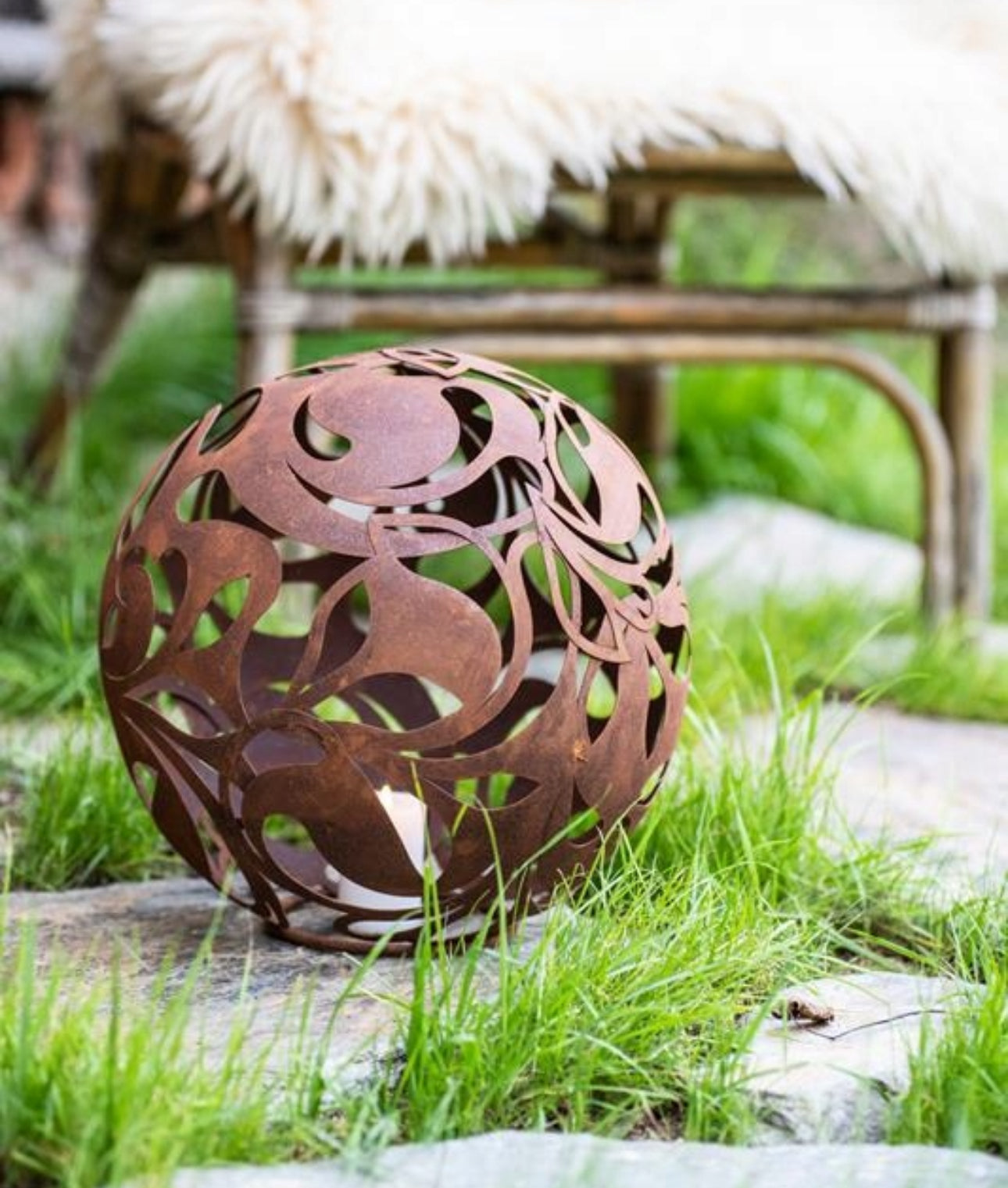 Rustikk metalllykt plassert i gress foran rottingstol i hage