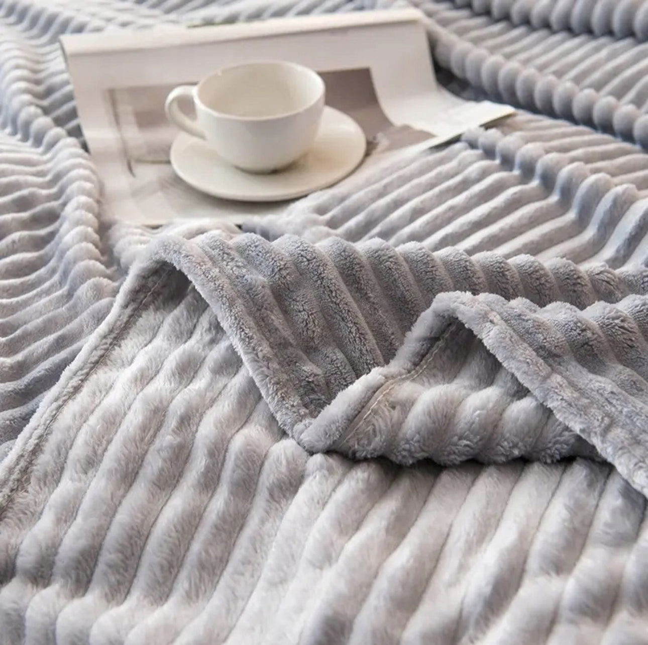 Nærbilde av lysgrått pledd med stripemønster og kaffekopp på brett