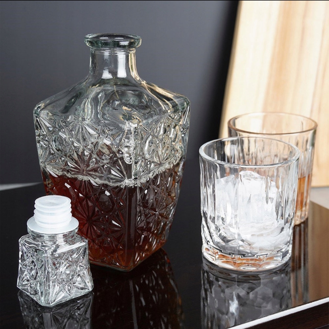 Glasskaraffel med mørk drikke sammen med whiskyglass på blank overflate