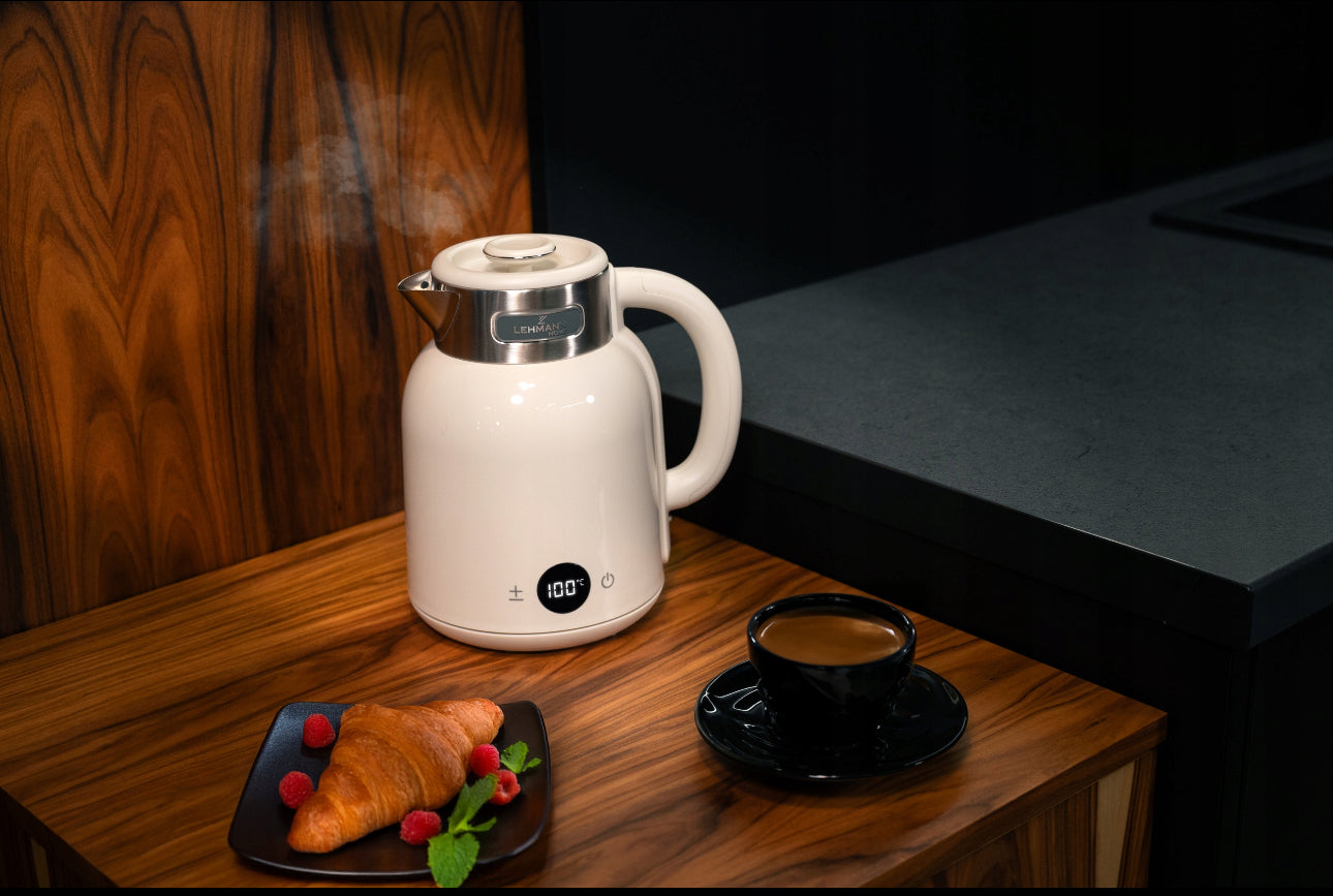 Hvit vannkoker med temperaturdisplay plassert på mørkt kjøkken med croissant og kaffe