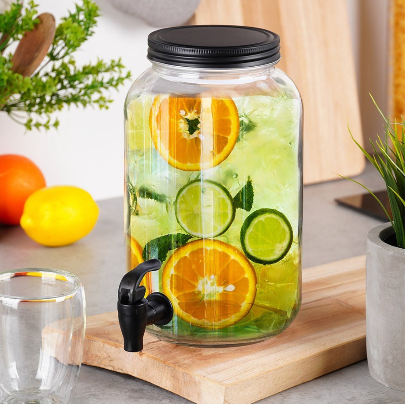 Glassdispenser med sitrusvann på kjøkkenbenk omgitt av frukt og planter