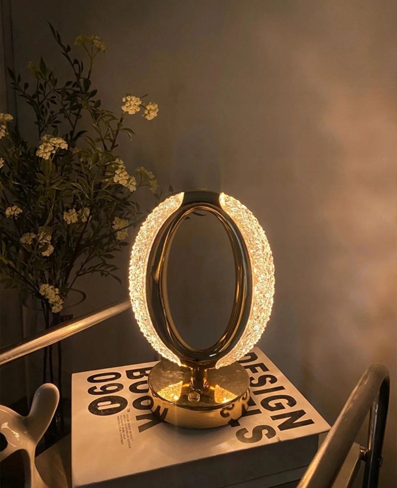 Elegant krystall lampe i gull plassert på bokhylle med dekorative blomster