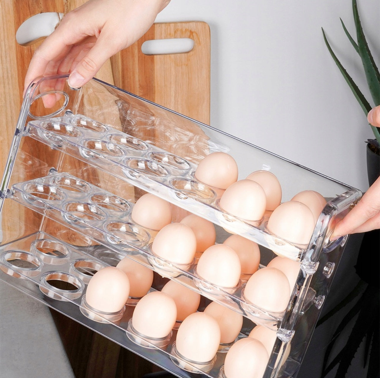Hender som løfter et eggstativ i gjennomsiktig plast fylt med egg