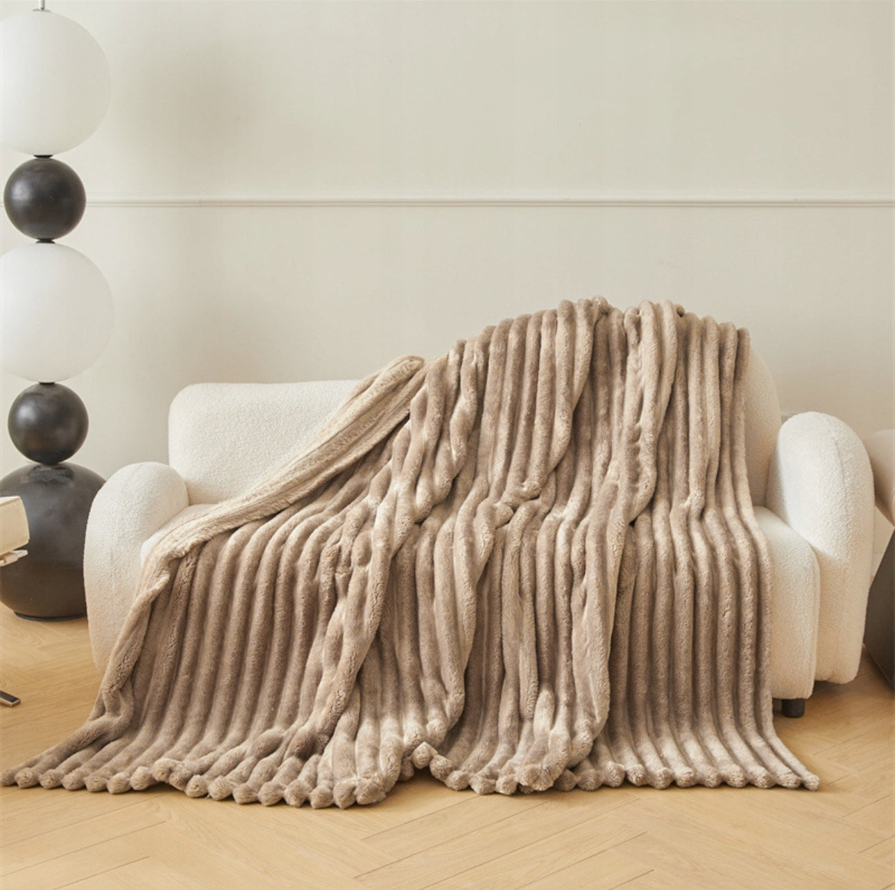Beige pledd i myk mikrofiber og 3D-struktur på lys sofa