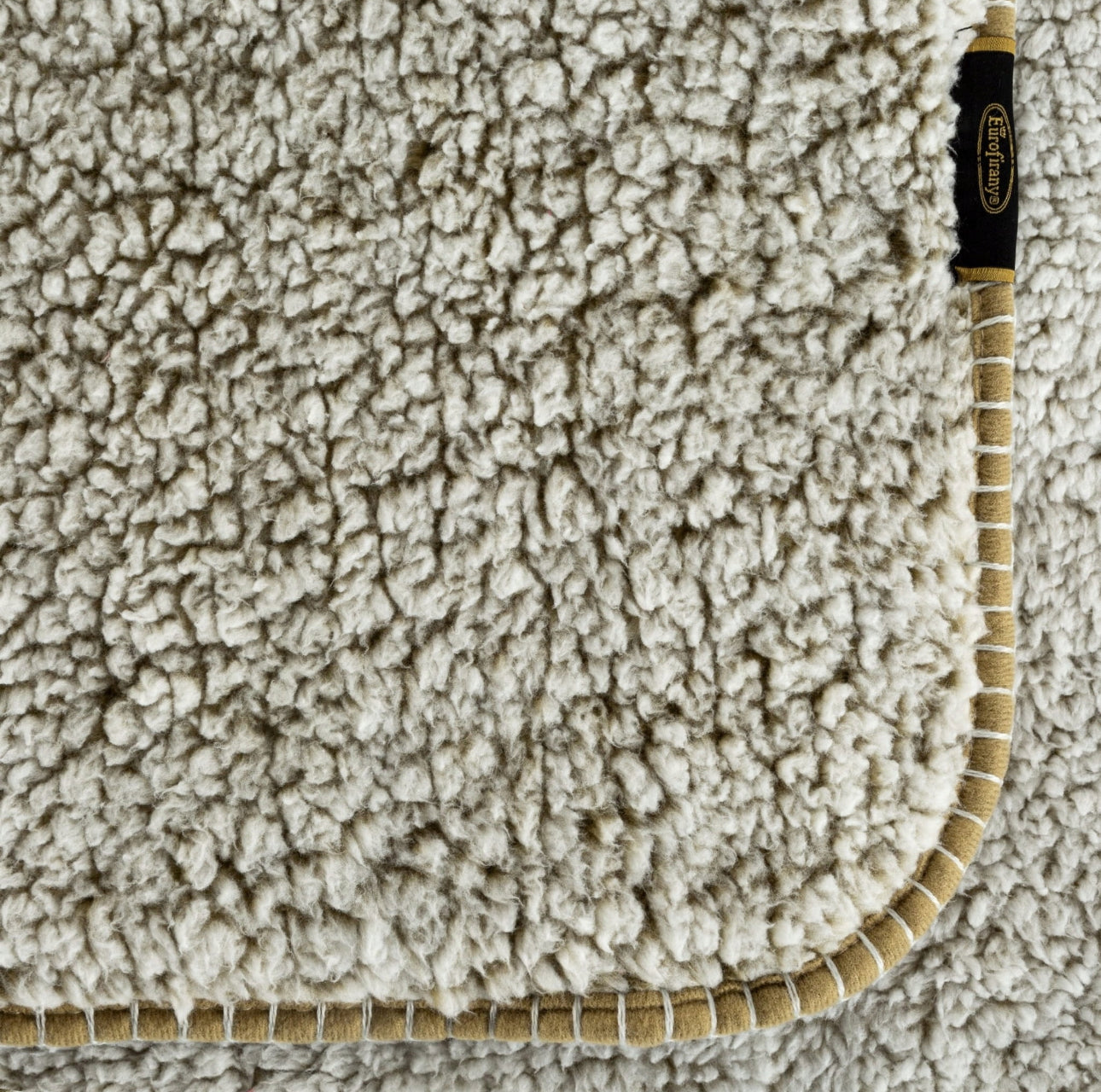 Hjørne av pledd med beige kant og synlig struktur i bouclé-materiale