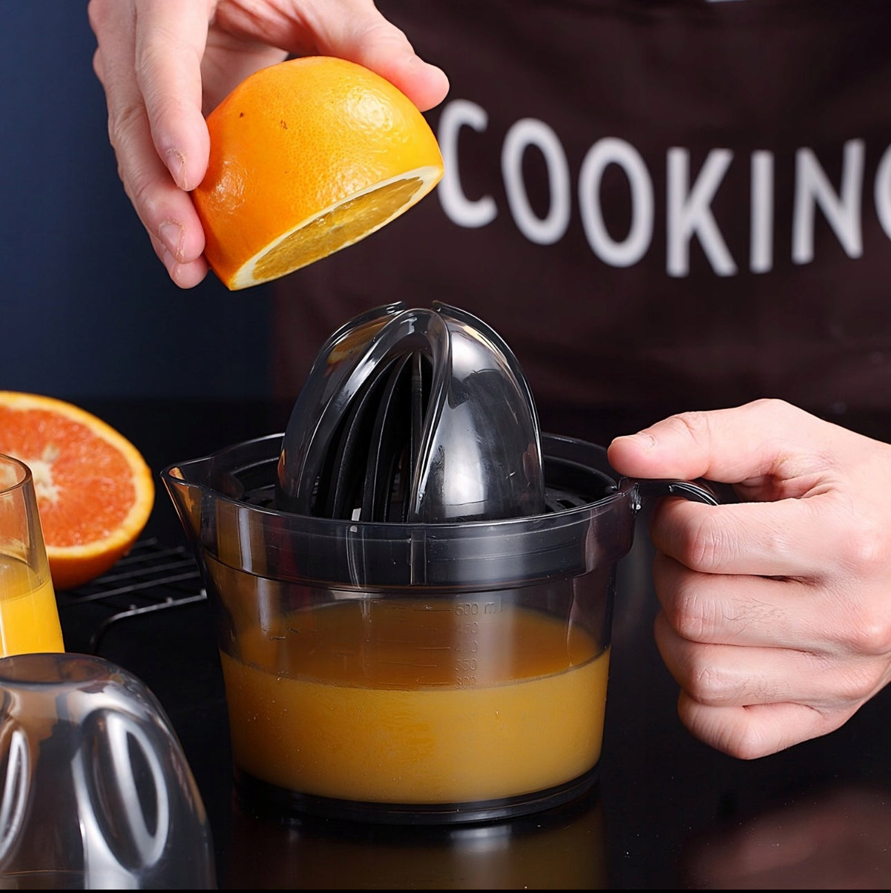 Person holder halv appelsin over sort sitruspresse med ferdigpresset juice i beholderen.