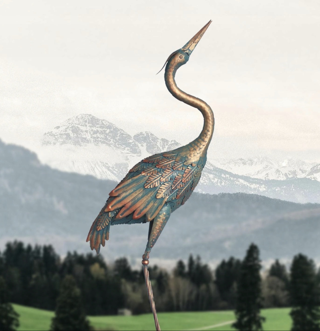 Slank metalltrane i blå og kobbernyanser, plassert med fjellandskap i bakgrunnen.