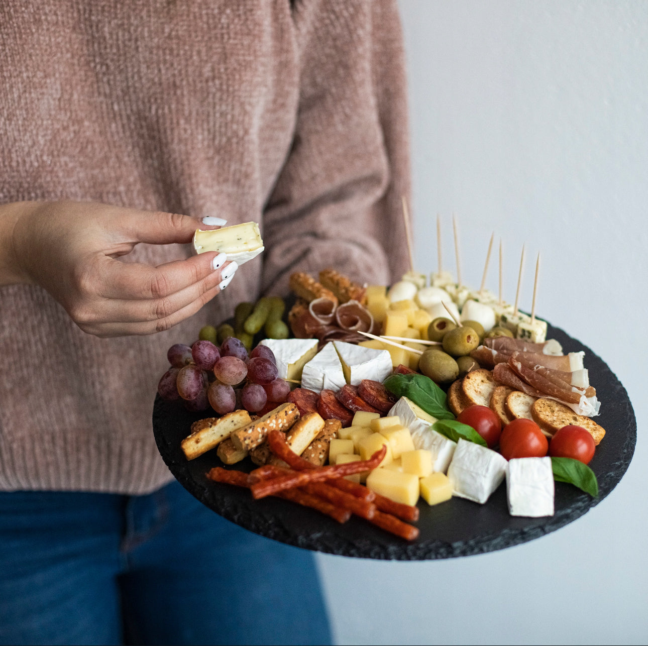 Person i genser holder serveringsfat med ost, chorizo og grønnsaker