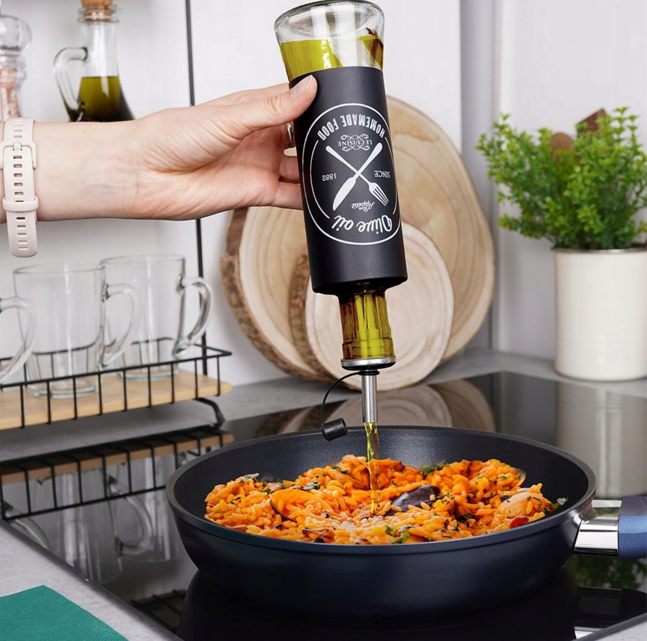 Hånd heller olje fra flaske over pastarett på kokeplate med sort stekepanne