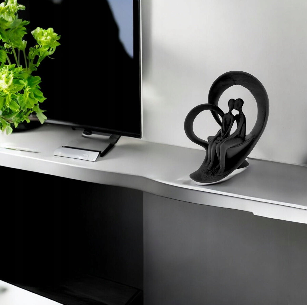 Svart romantisk skulptur på hvit TV-benk ved siden av grønn plante