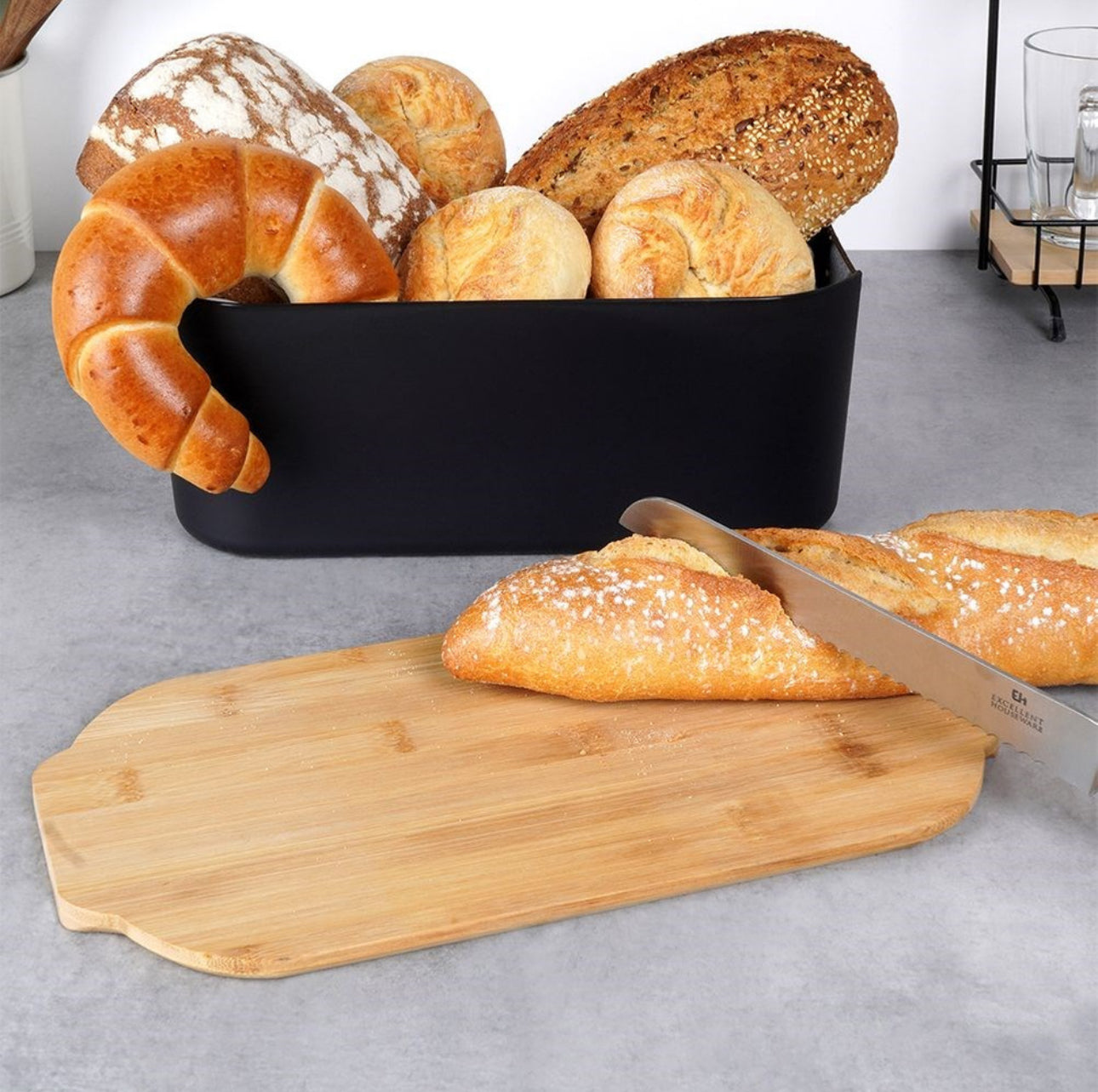 Brødboks fylt med ulike brødtyper og croissanter ved siden av skjærebrett