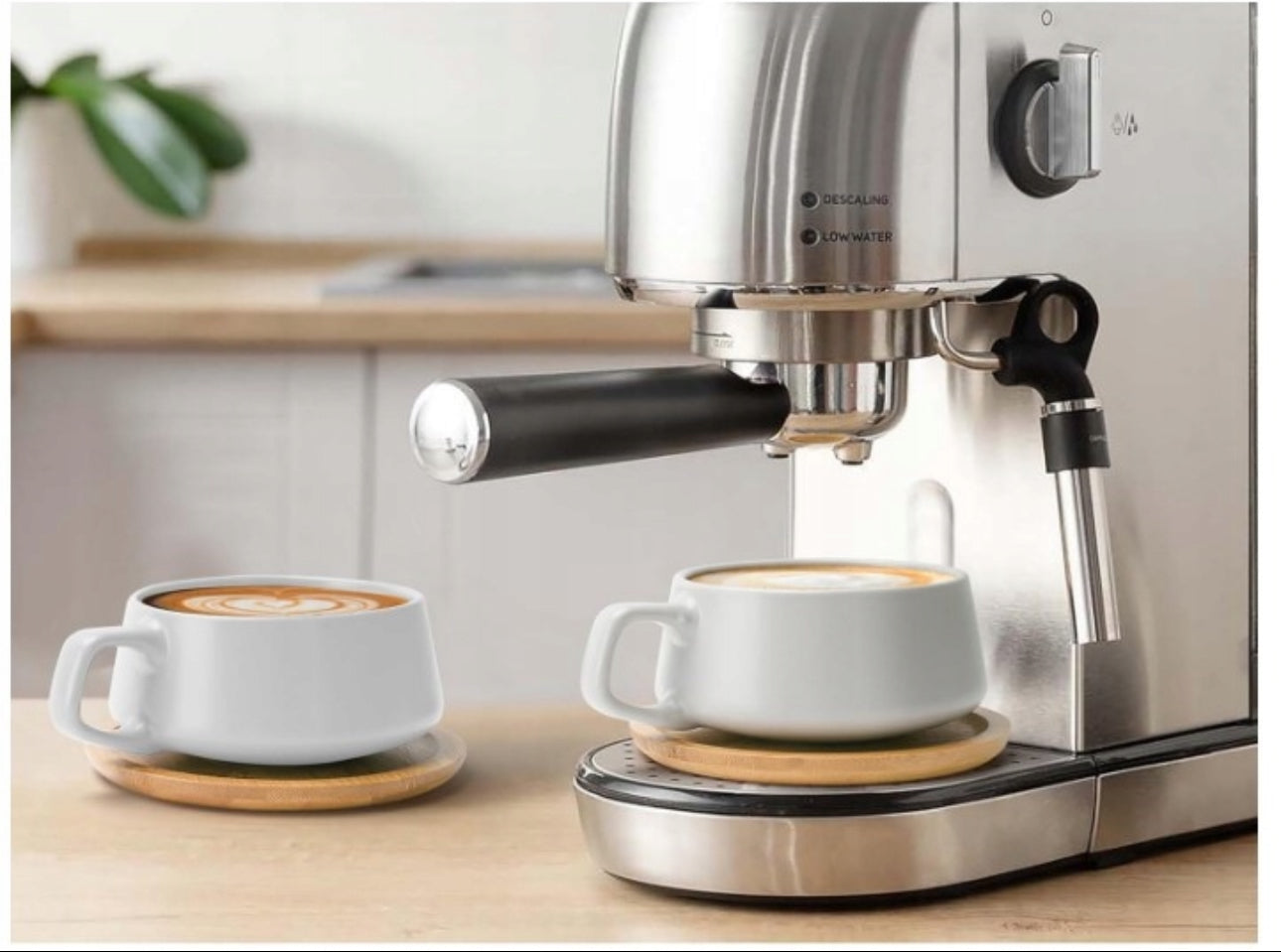 To hvite keramiske kopper med bambusunderlag under espressomaskin på kjøkkenbenk