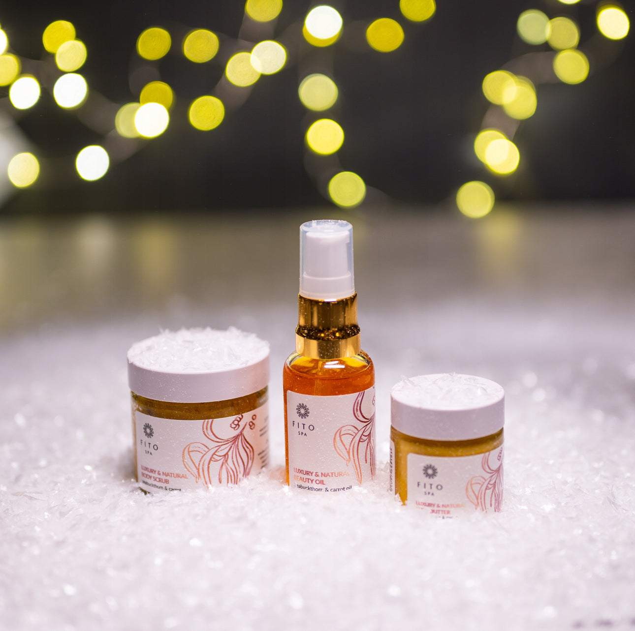 Hudpleiesett med gyldne produkter plassert i snø med bokeh-lys i bakgrunnen