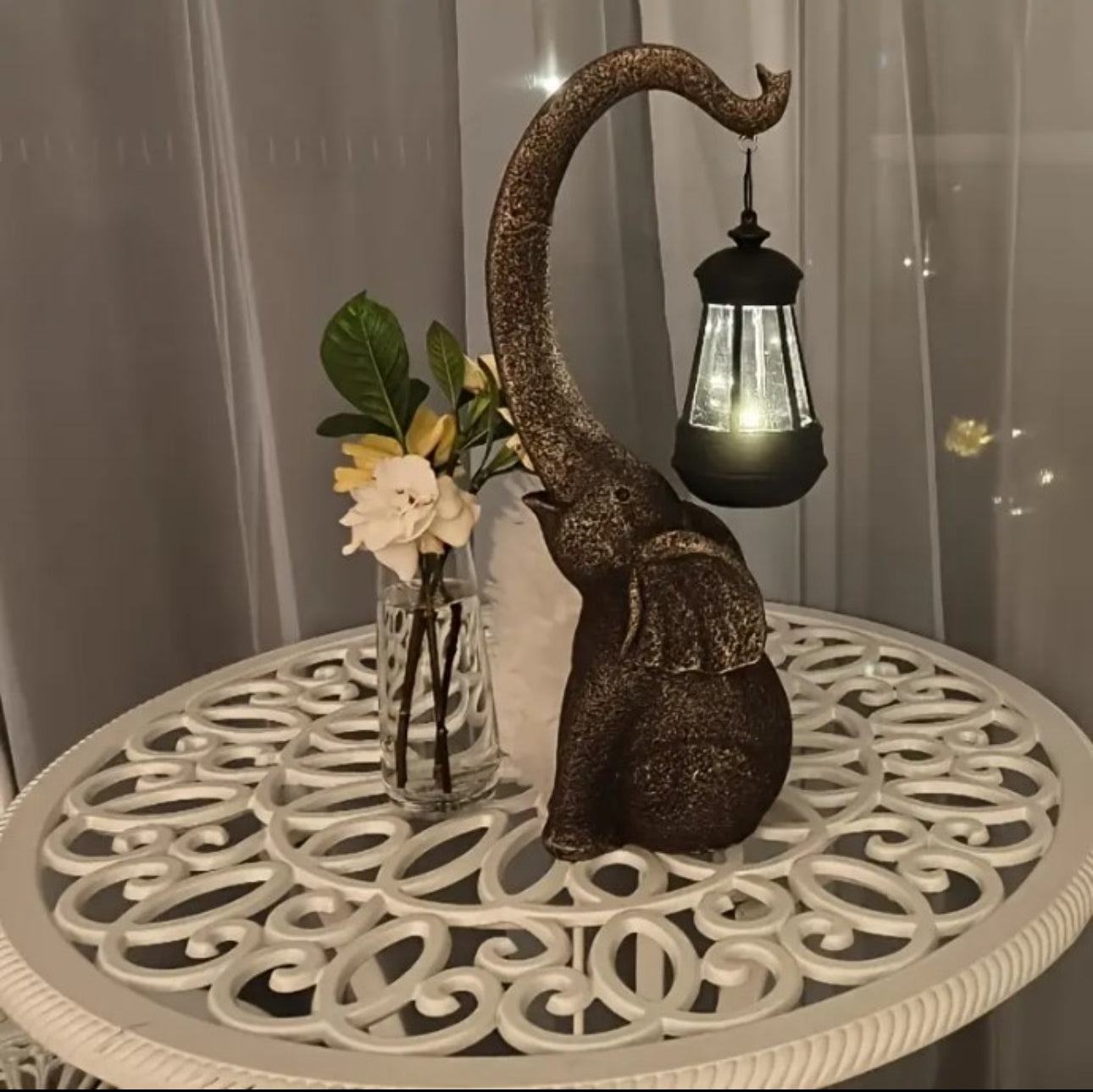 Elefantfigur med solcelledrevet LED-lykt på hvitt hagebord ved siden av blomster i vase innendørs