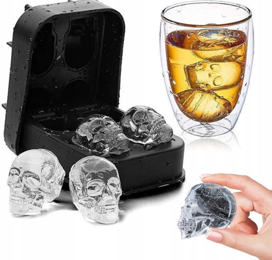Silikonform i svart med fire hodeskalleformede isbiter ved siden av et glass med drink og isformede hodeskaller.
