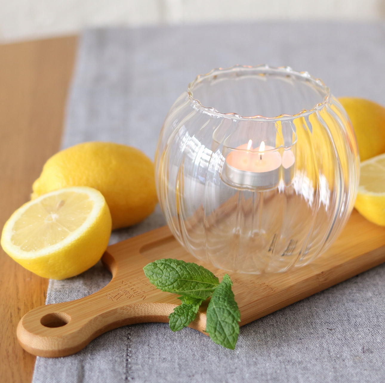Riflet telysholder i klart glass med tent lys, dekorert med sitroner og urter