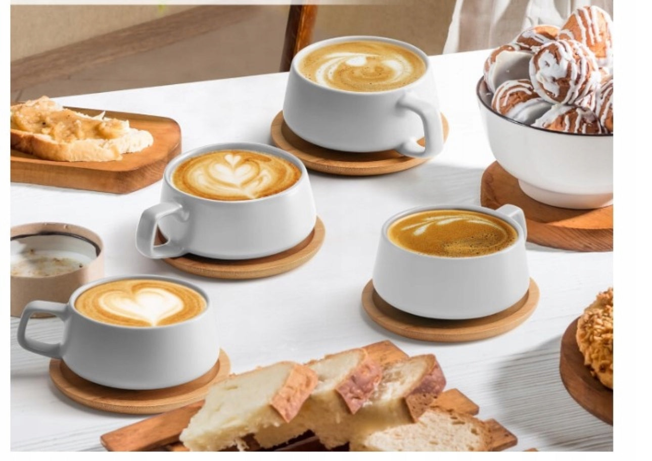 Hvite cappuccinokopper med bambusunderlag servert med kaffe og bakverk på bord