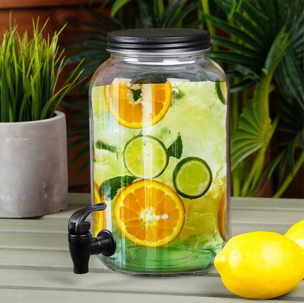 Glassdispenser med sitrusvann plassert på utebord med sitroner og planter