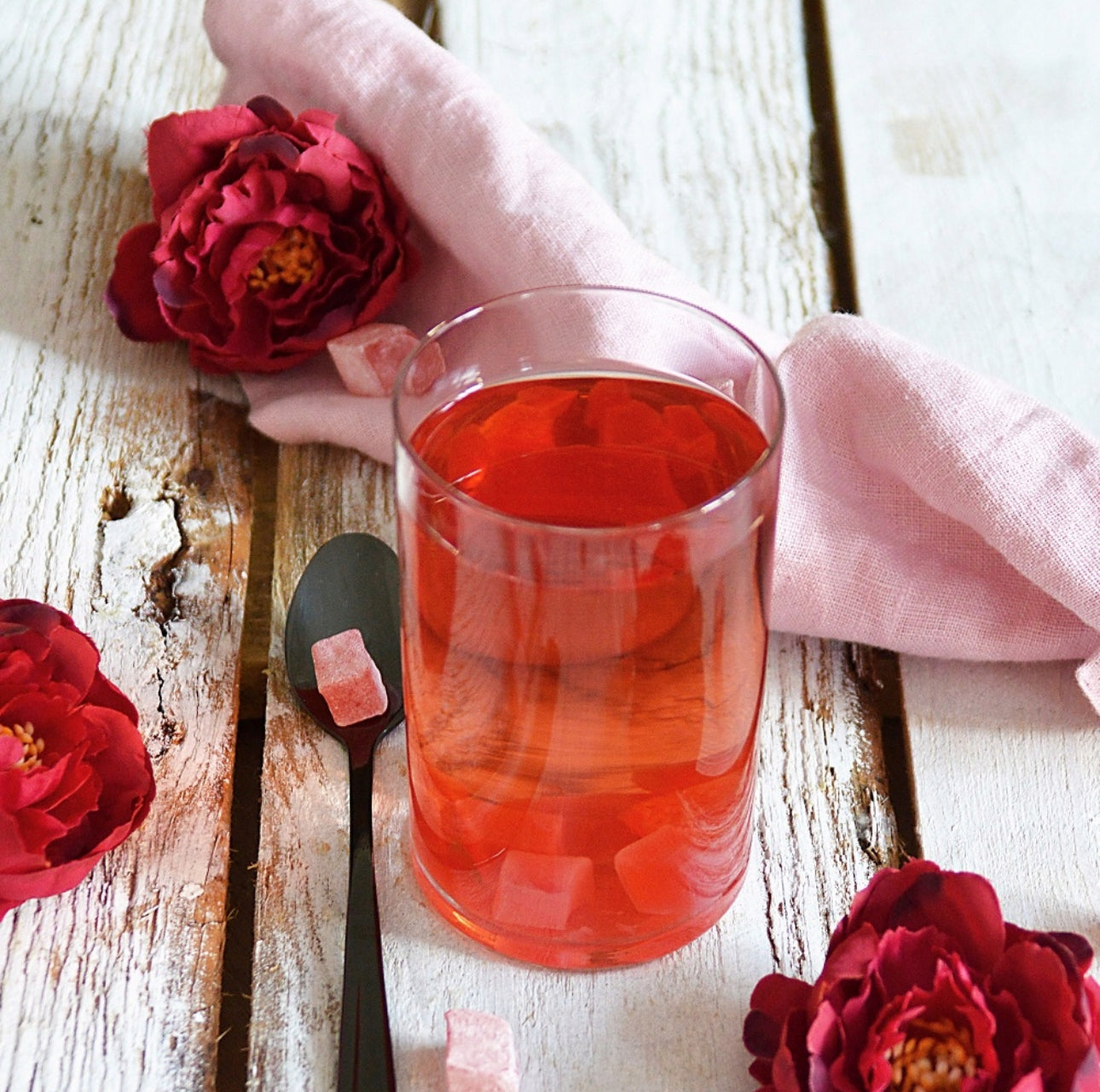 Glass med rød drikk, omgitt av blomster og rosa serviett
